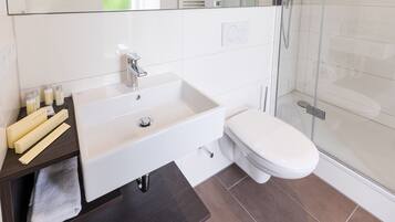 Un bany modern amb un lavabo blanc, un vàter i una cabina de dutxa de vidre.