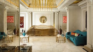 Un salón lujoso con una zona de estar central, un reloj de pared grande y un techo alto con lámparas colgantes.