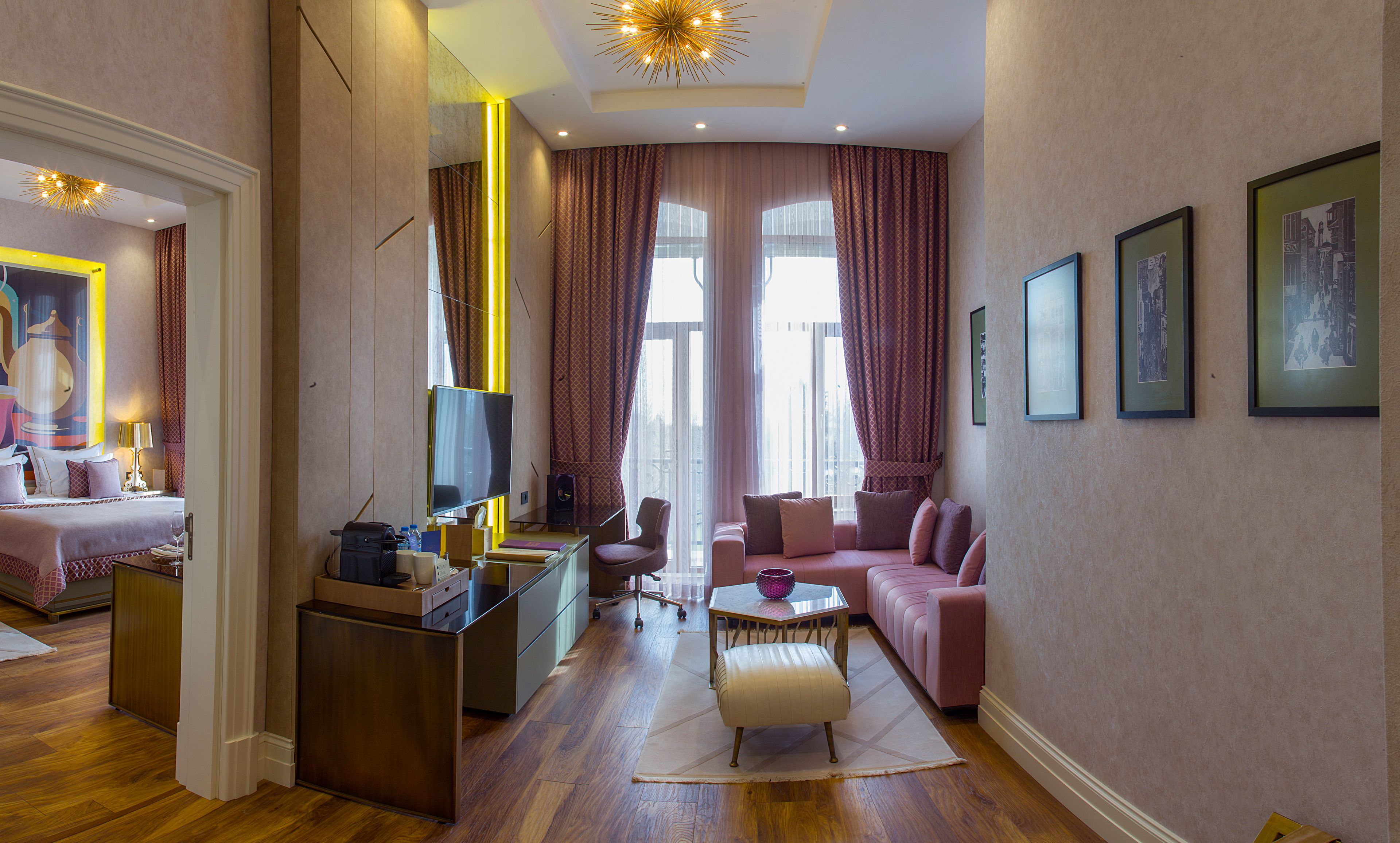 A modern hotel room with a bed, a desk, a sofa, and a dining area.