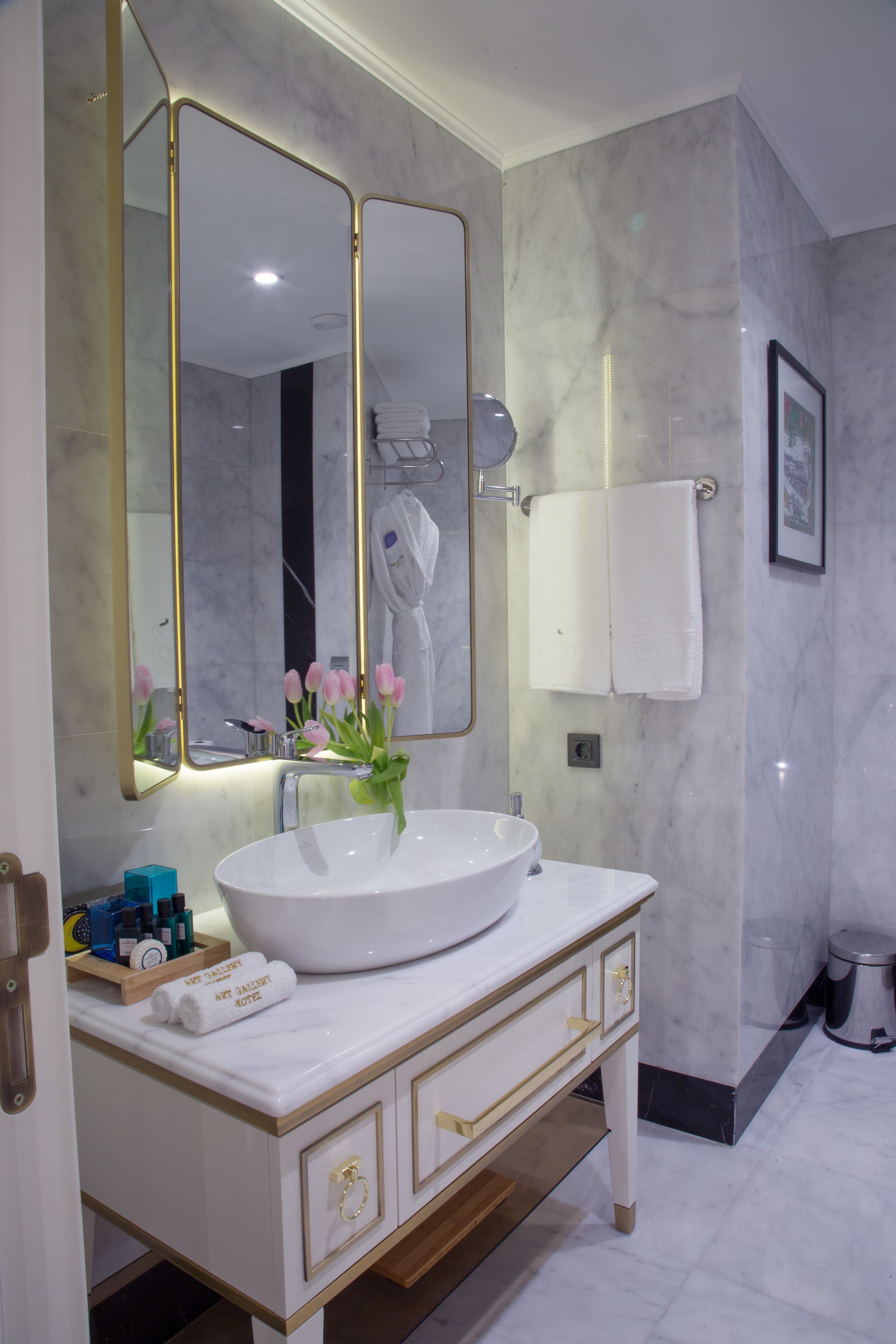 A bathroom with a white sink, gold-toned cabinet, and a large mirror with gold trim.