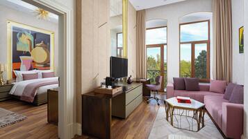 Een hotelkamer met een bed, een bureau met televisie, een bank en grote ramen met uitzicht op de omgeving.