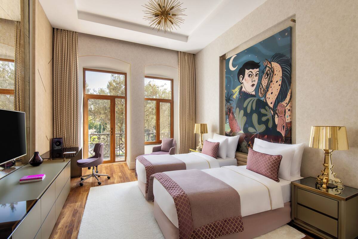 Een hotelkamer met twee bedden, een bureau met een televisie en grote ramen.
