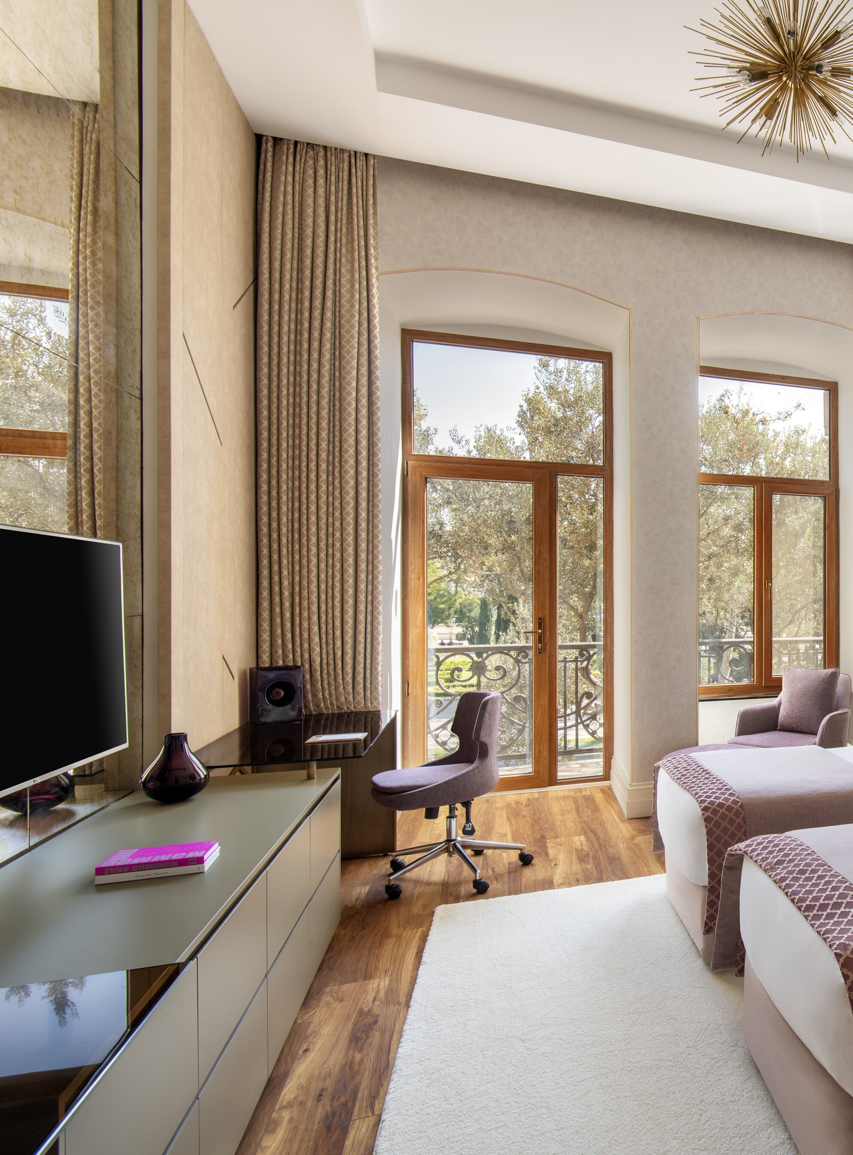 A modern hotel room with a large window, a desk with a computer, a chair, and a bed.