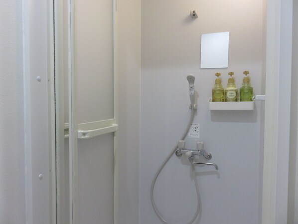 A bathroom with a shower, a white shelf with three bottles, and a small whiteboard on the wall. - Pirka Sapporo - Hostel (Sapporo)