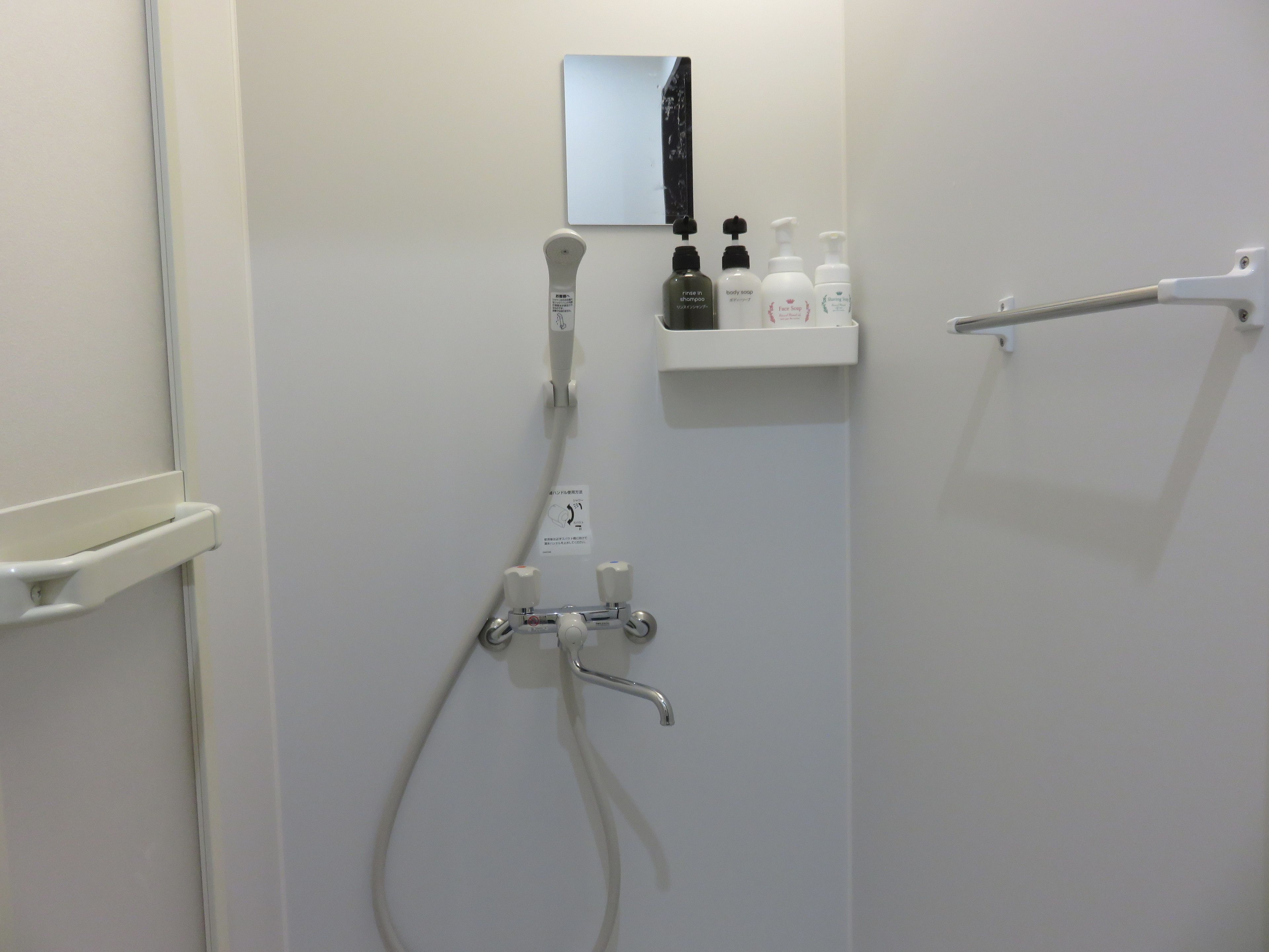A bathroom with a shower, a mirror, and a shelf with toiletries.