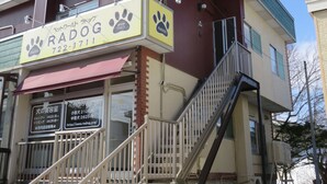 A building with a sign for 'RADOG' featuring paw prints and a phone number. There are stairs leading to a balcony. - Pirka Sapporo - Hostel (Sapporo)