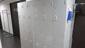 A row of grey lockers with numbers and letters on them, a mop and a hanger on the left, and a blue bottle on the right. - Pirka Sapporo - Hostel (Sapporo)