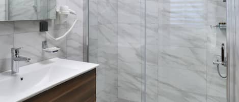 Un baño moderno con ducha revestida de mármol, tocador con espejo y un perchero para toallas.
