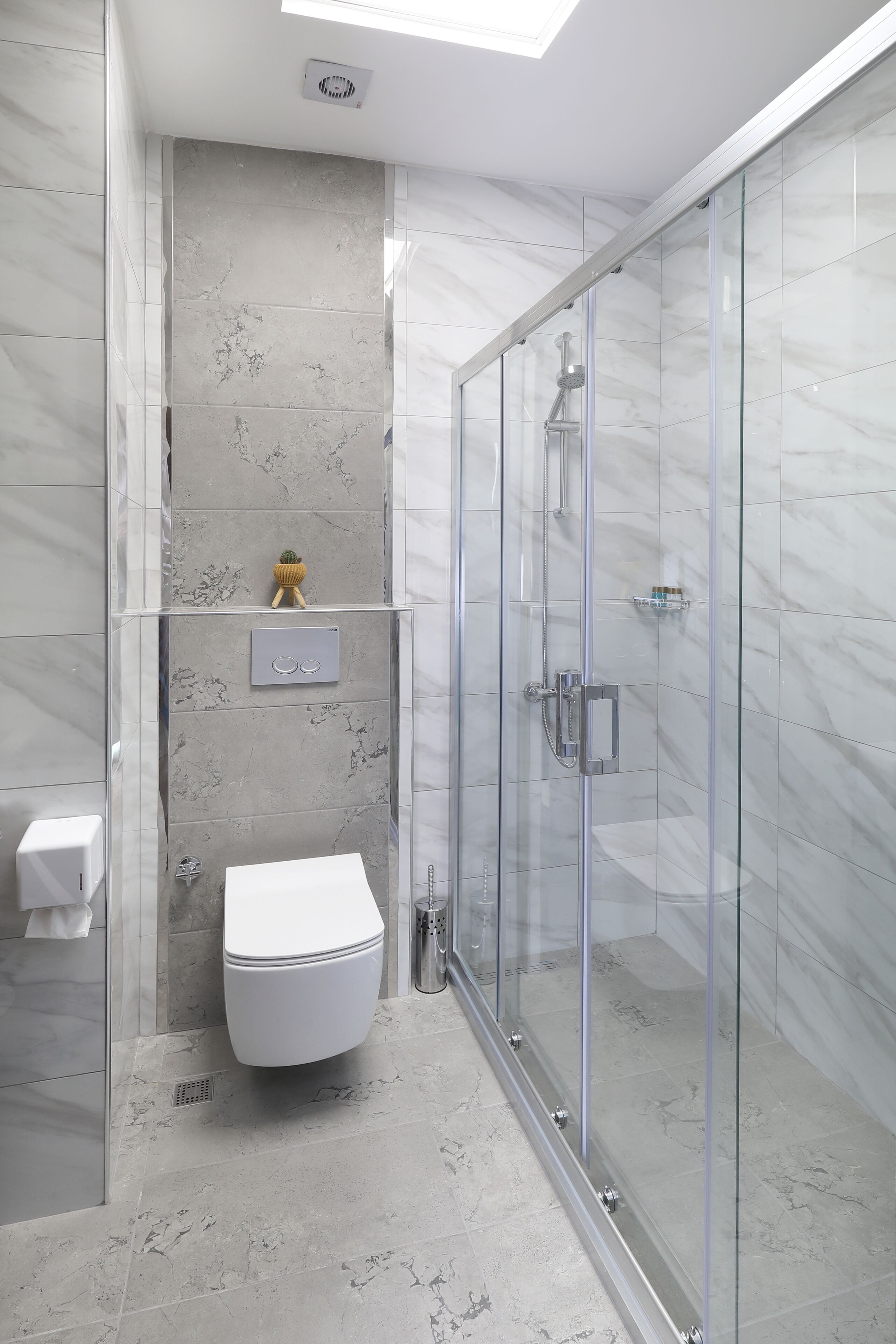 A modern bathroom with a glass-enclosed shower, a toilet, and a marble-tiled wall.