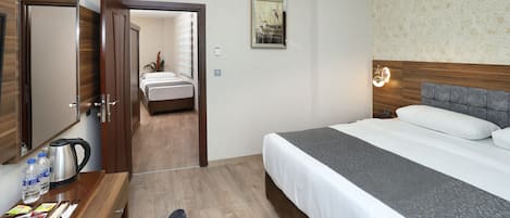 Habitación de hotel con cama, escritorio con hervidor, botellas de agua y espejo.