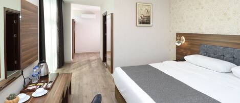 Una habitación de hotel con una cama, un escritorio con silla, una cafetera y un pequeño cactus en la mesa.