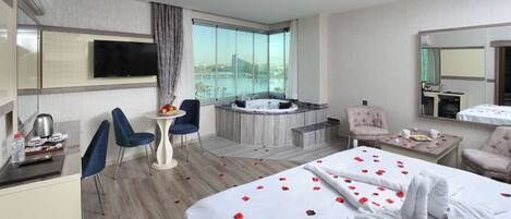 Habitación de hotel con cama, escritorio, silla, mesita, bañera y ventana grande con vista a la ciudad.