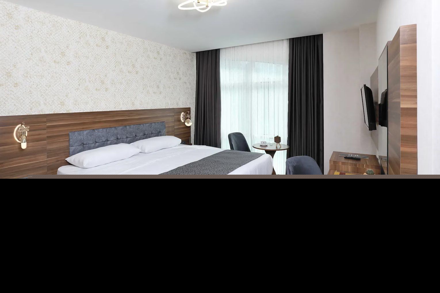 A hotel room with a large bed, bedside tables, a desk with a chair, a television, and a window with curtains.