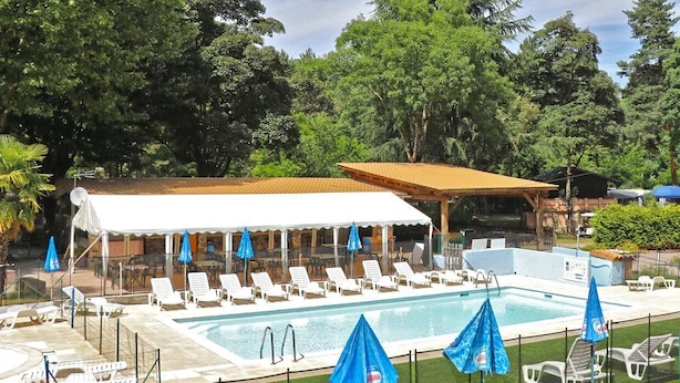 Un área de piscina con sillas de descanso y sombrillas, rodeada de árboles.