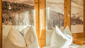 Ein gemütliches Zimmer mit Bett, Kissen und einer Holzwand mit Blick auf die Berge.
