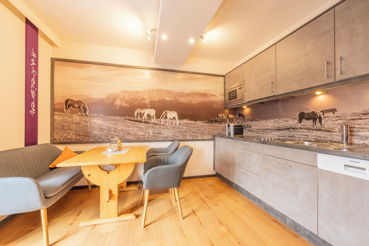 A modern kitchen with a wooden dining table and chairs, a large wall mural of horses, and built-in appliances.