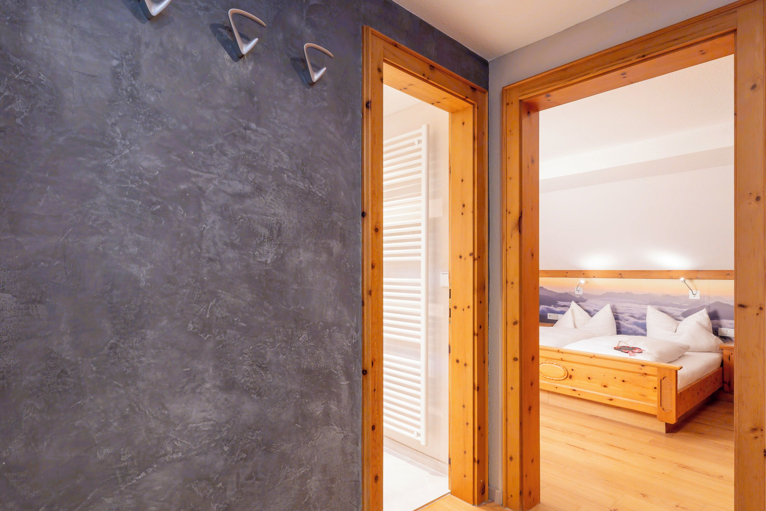 A bedroom with a wooden bed, a grey wall, and a wooden door leading to another room.