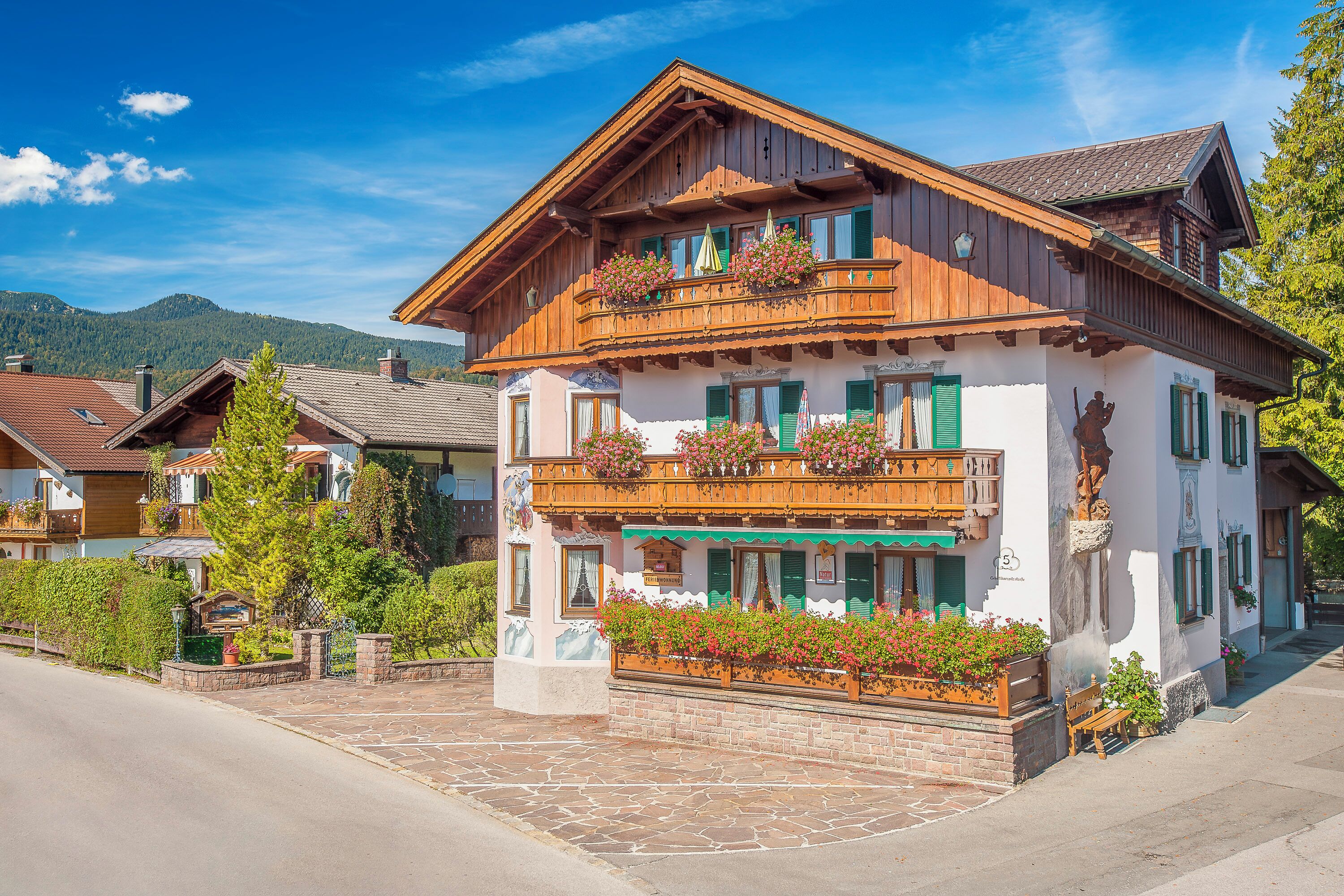 Ein traditionelles Gebäude im alpinen Stil mit Holzfassade, Balkonen mit Blumenkästen und einem pflasterbelagten Eingang.