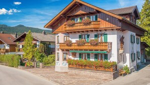 Ein traditionelles Gebäude im alpinen Stil mit Holzfassade, Balkonen mit Blumenkästen und einem pflasterbelagten Eingang.