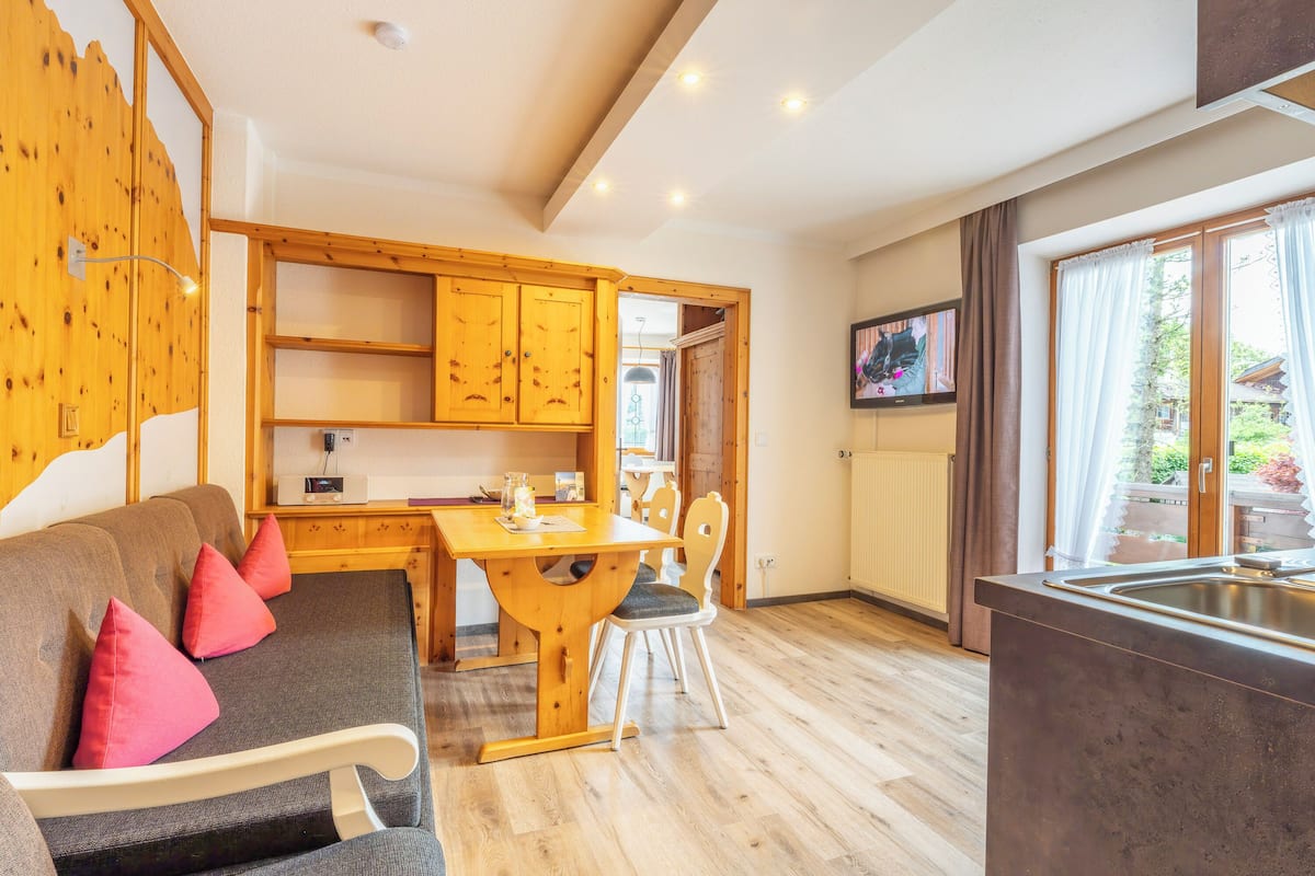 A cozy room with a sofa, a wooden dining table, and a kitchen area.