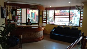 Un espace d’accueil comprenant un comptoir de réception, un panneau d’identification, un coin salon avec un canapé et une vue sur la rue grâce à de grandes fenêtres.