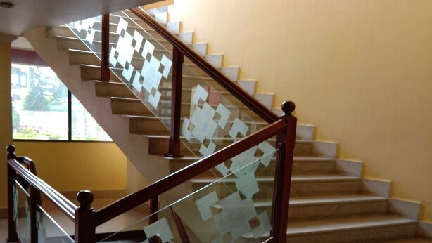 Un escalier avec une rampe en bois et des panneaux de verre, menant à un palier d’où l’on peut admirer la vue sur l’extérieur.