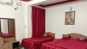 Une chambre avec deux lits, chacun recouvert d’une couverture rouge assortie à ses oreillers. On y trouve une tête de lit en bois, un miroir et une petite armoire en bois.