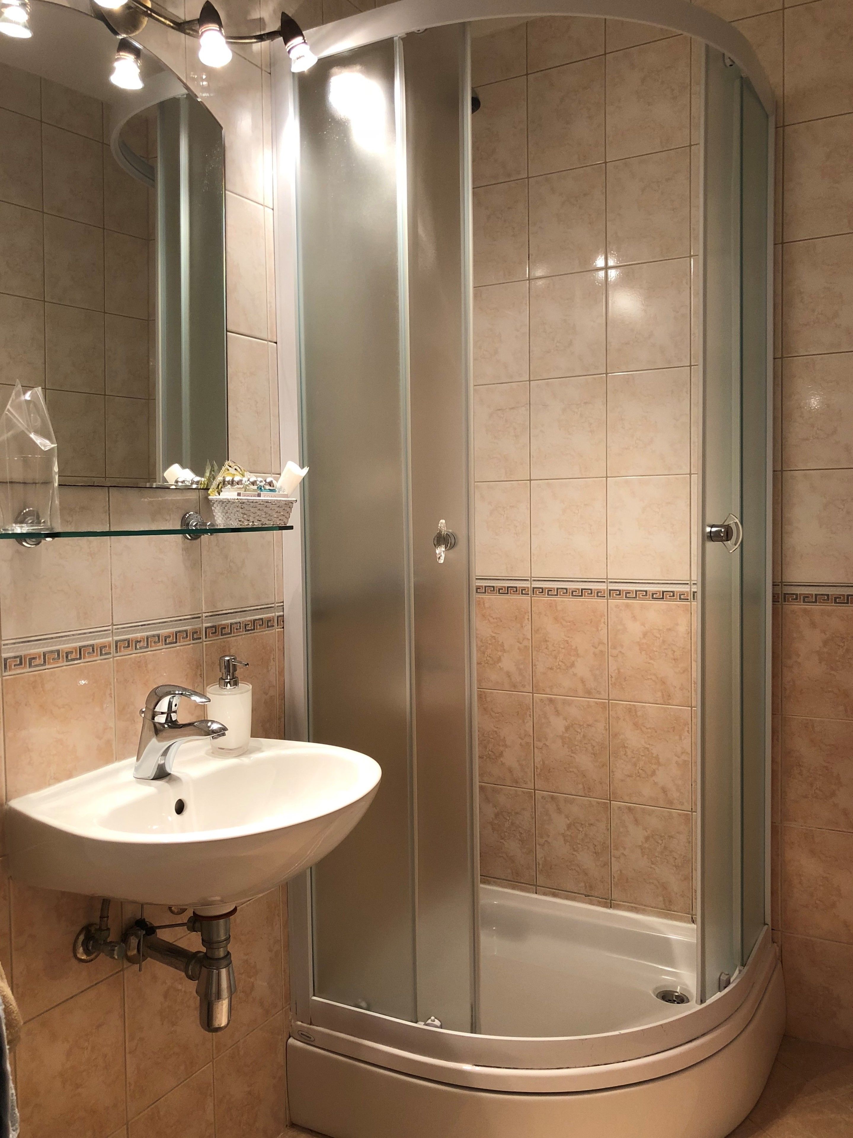 Un baño con ducha envuelta en vidrio, un lavabo con espejo y un borde decorativo de azulejos.