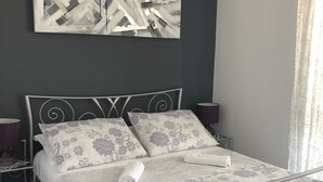 Ein ordentlich bezogenes Bett mit floralem Bettzeug, einem modernen Metall-Kopfteil und einem zeitgenössischen abstrakten Gemälde darüber.