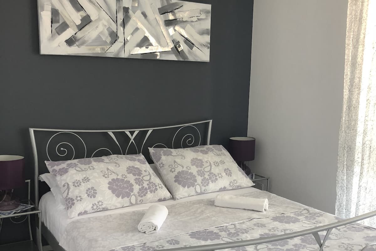 Cama bem arrumada com roupa de cama estampada em flores, cabeceira de metal moderna e uma pintura abstrata contemporânea acima.