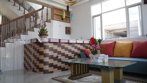 A modern living room with a glass coffee table, a blue sofa with red and yellow cushions, and a staircase with a patterned wall. - See Starsea Guest House (Magong)