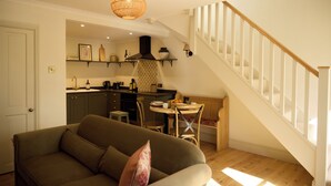 Ein Wohnzimmer mit Sofa, einem Esstisch mit Stühlen, einer Küchenzeile und einer Treppe.