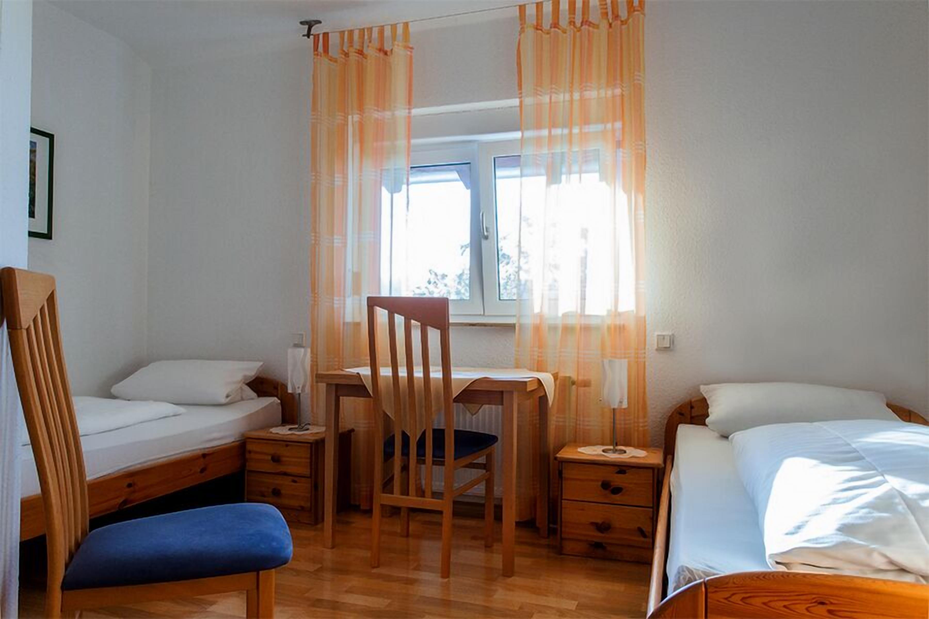 Ein Schlafzimmer mit Bett, Schreibtisch, Stuhl und einem Fenster mit Vorhängen.