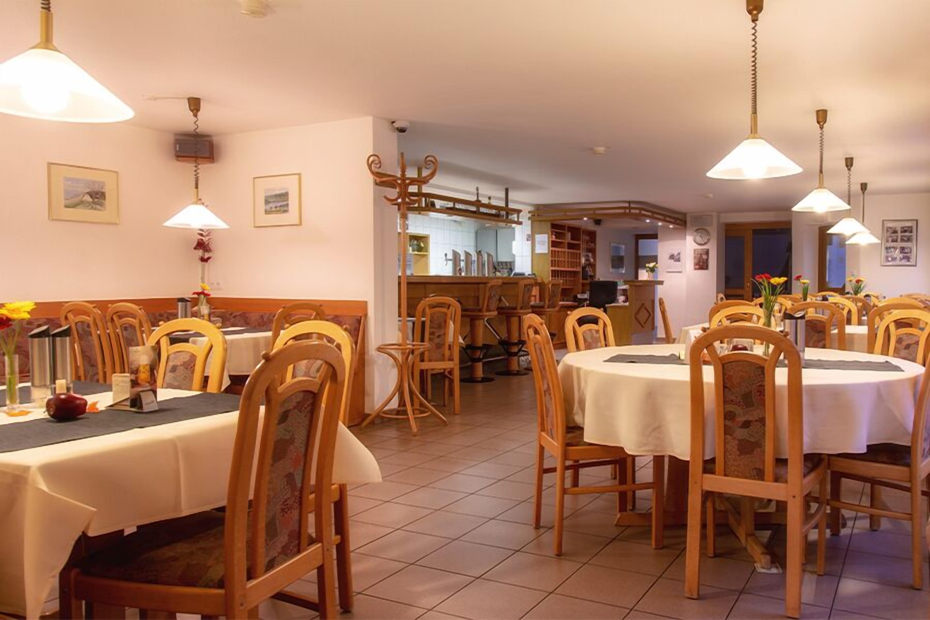 Zona pranzo con tavoli e sedie rotonde, una cucina sullo sfondo e lampade a sospensione.