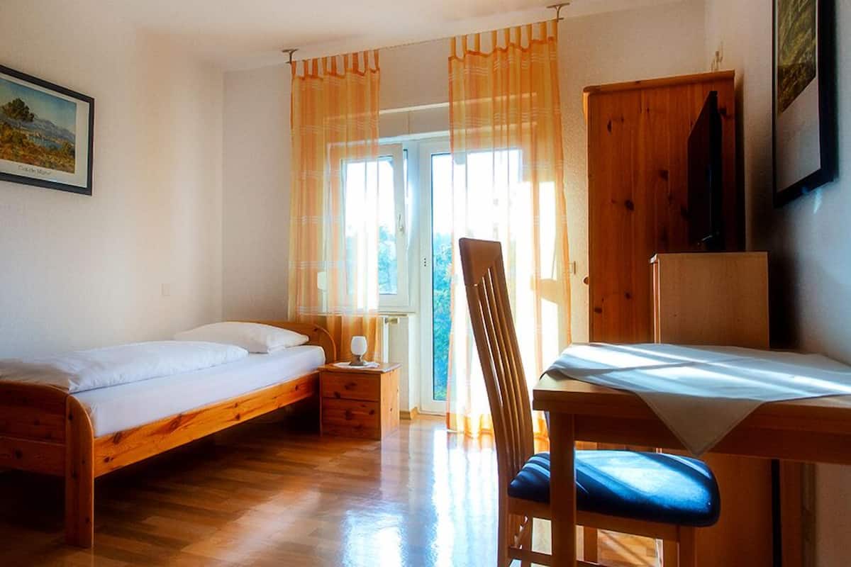 A room with a wooden bed, a desk with a chair, and a wardrobe.