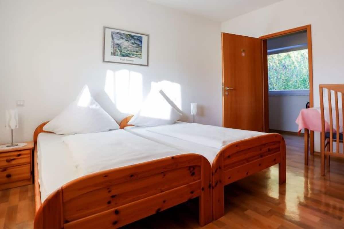 A bedroom with a wooden bed, a desk with a chair, a window, and a door.