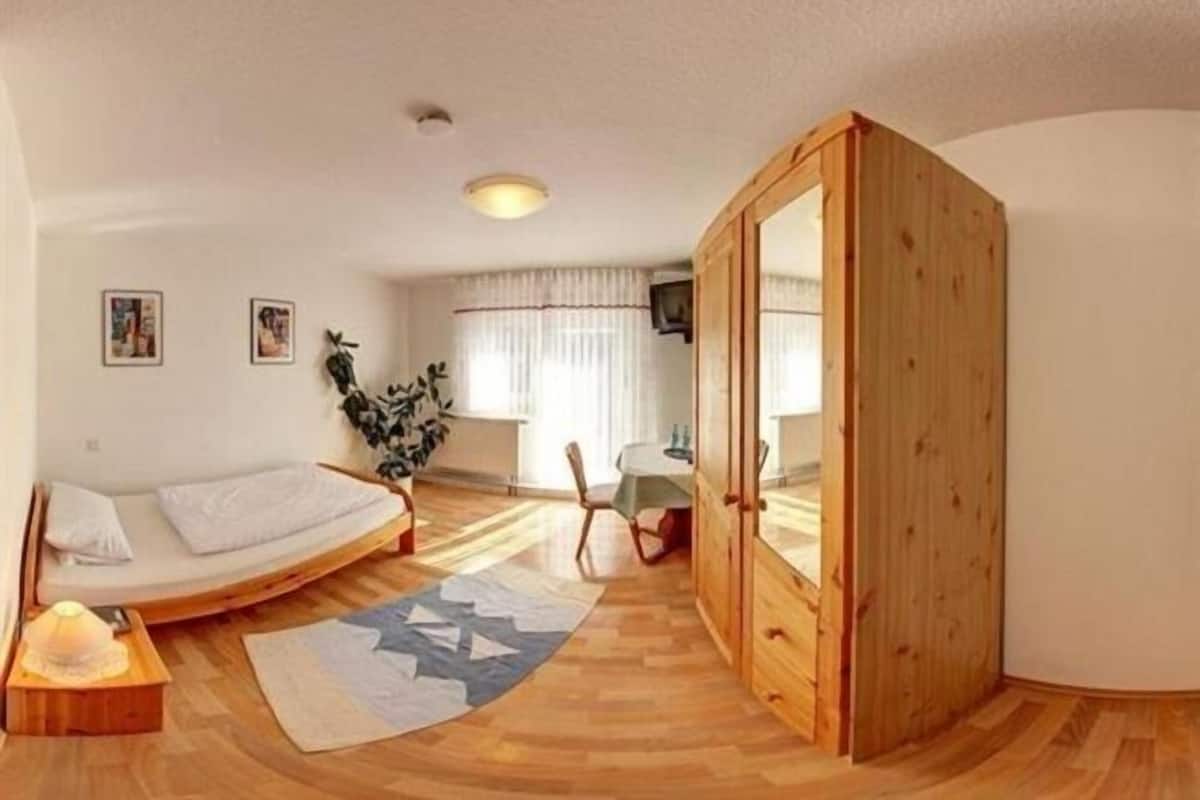 A compact bedroom with a bed, a wooden wardrobe, a small desk, and a chair.