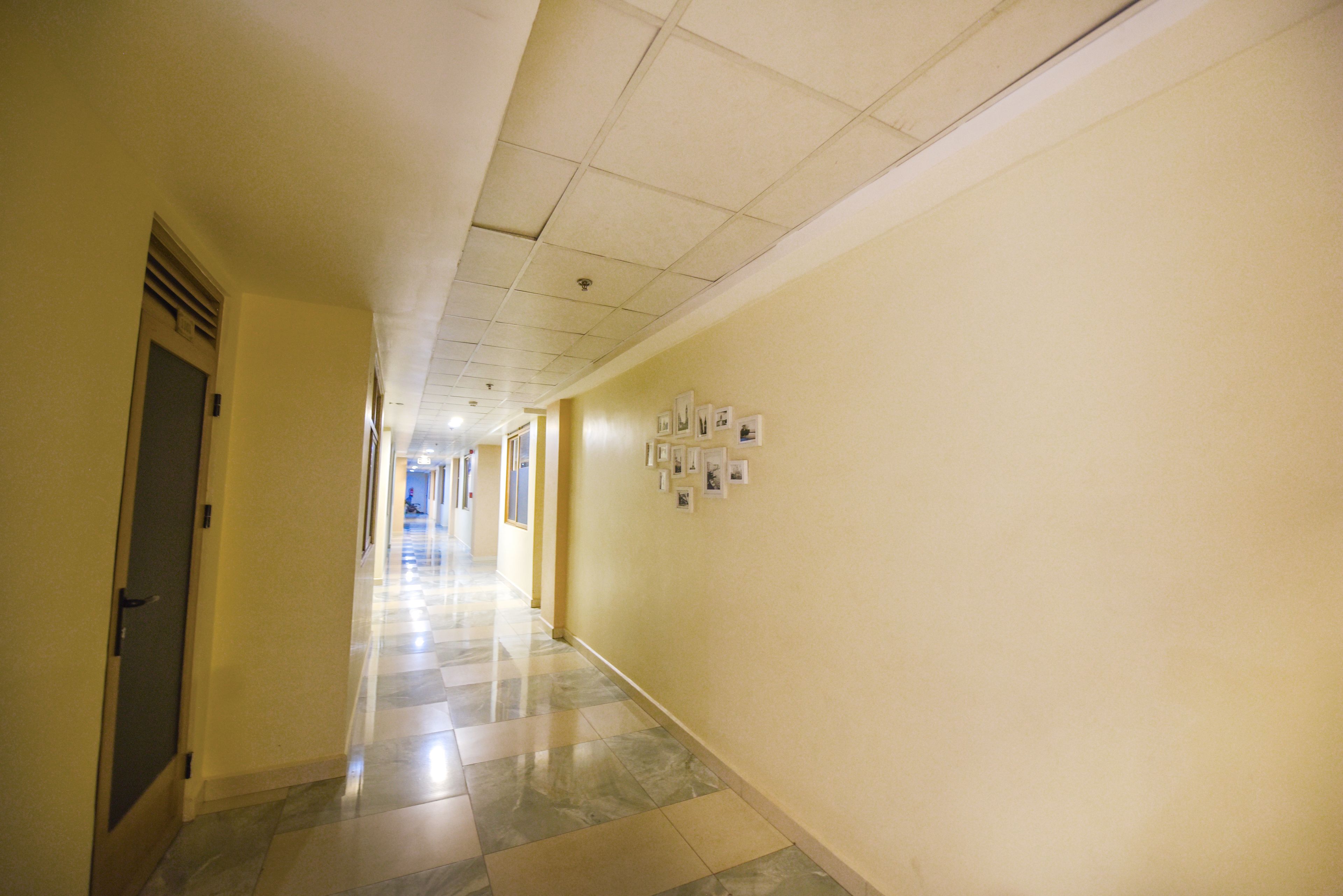 Um corredor com piso ladrilhado, uma porta à esquerda e uma parede com quadros à direita.