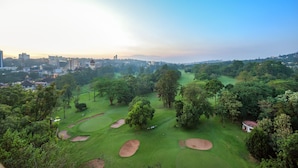 A golf course with bunkers, trees, and a city skyline in the background. - BMK House Apartments (Kampala)