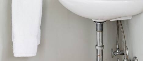 Un baño con lavamanos blanco, grifo cromado y una toalla colgada en un perchero metálico.