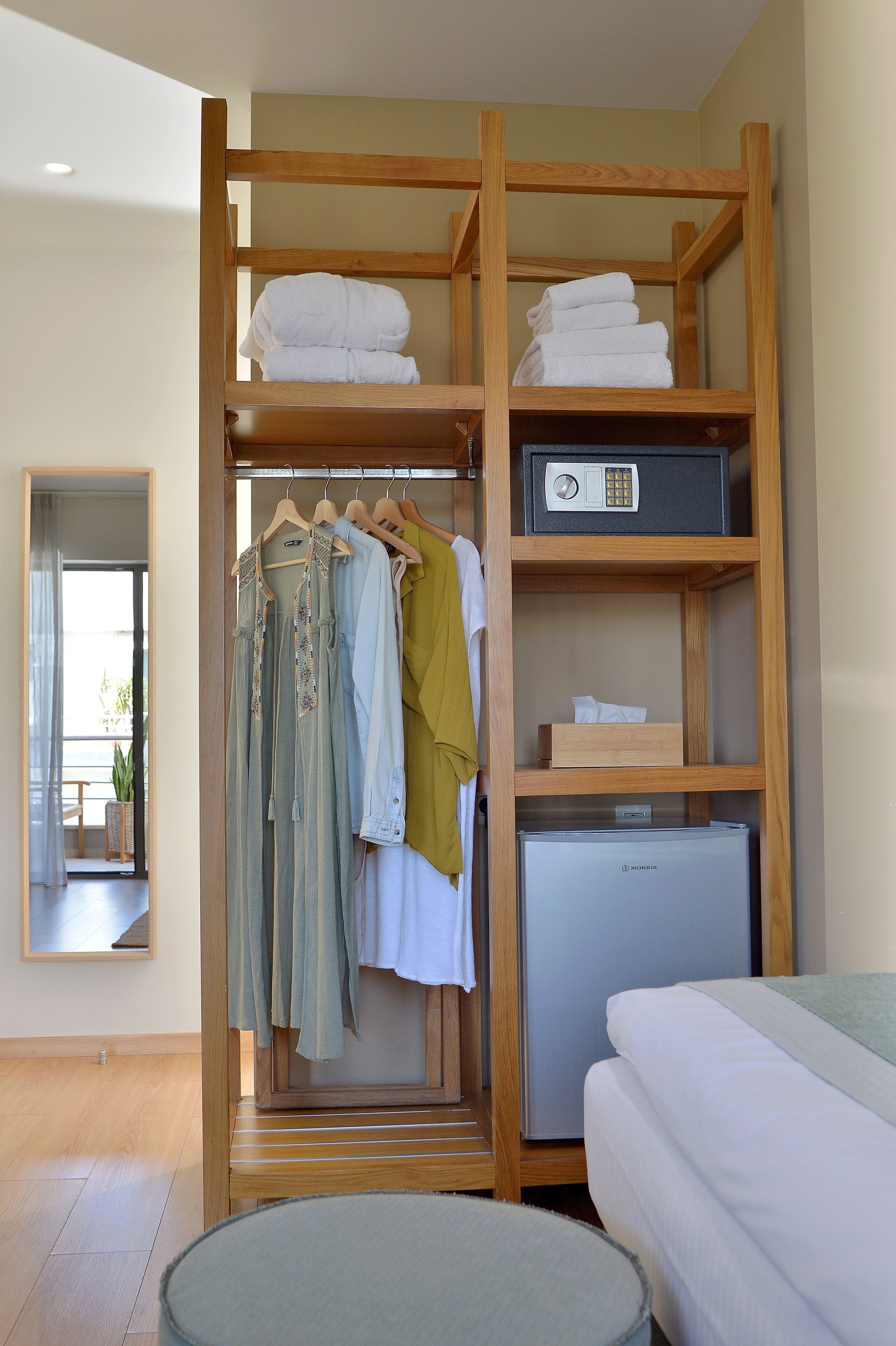 A hotel room with a wooden wardrobe, a bed, and a small refrigerator.
