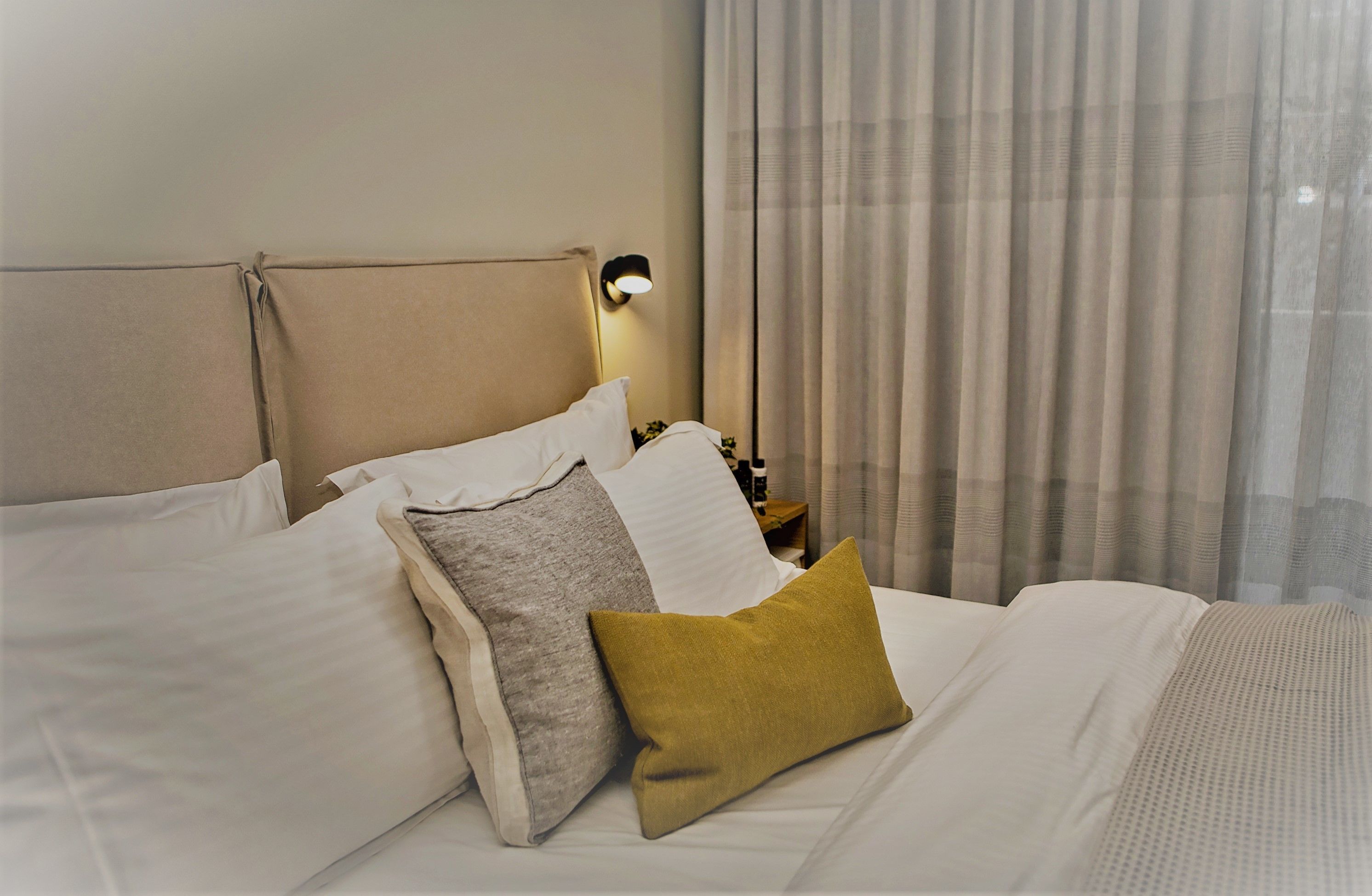 A neatly made bed with white and mustard pillows, a headboard, and a bedside lamp.