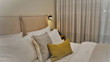 A neatly made bed with white and mustard pillows, a headboard, and a bedside lamp.