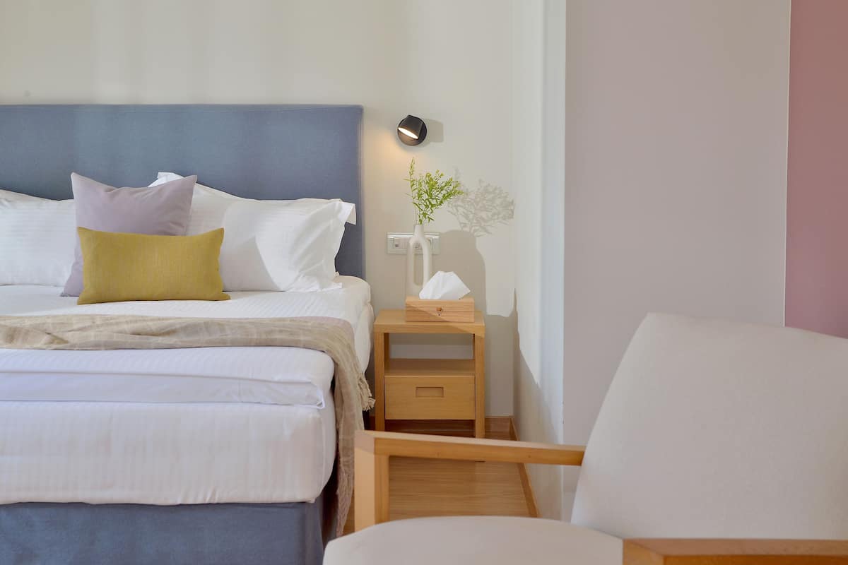 Een opgemaakt bed met meerdere kussens, een nachtkastje met zakdoekjes en een stoel.