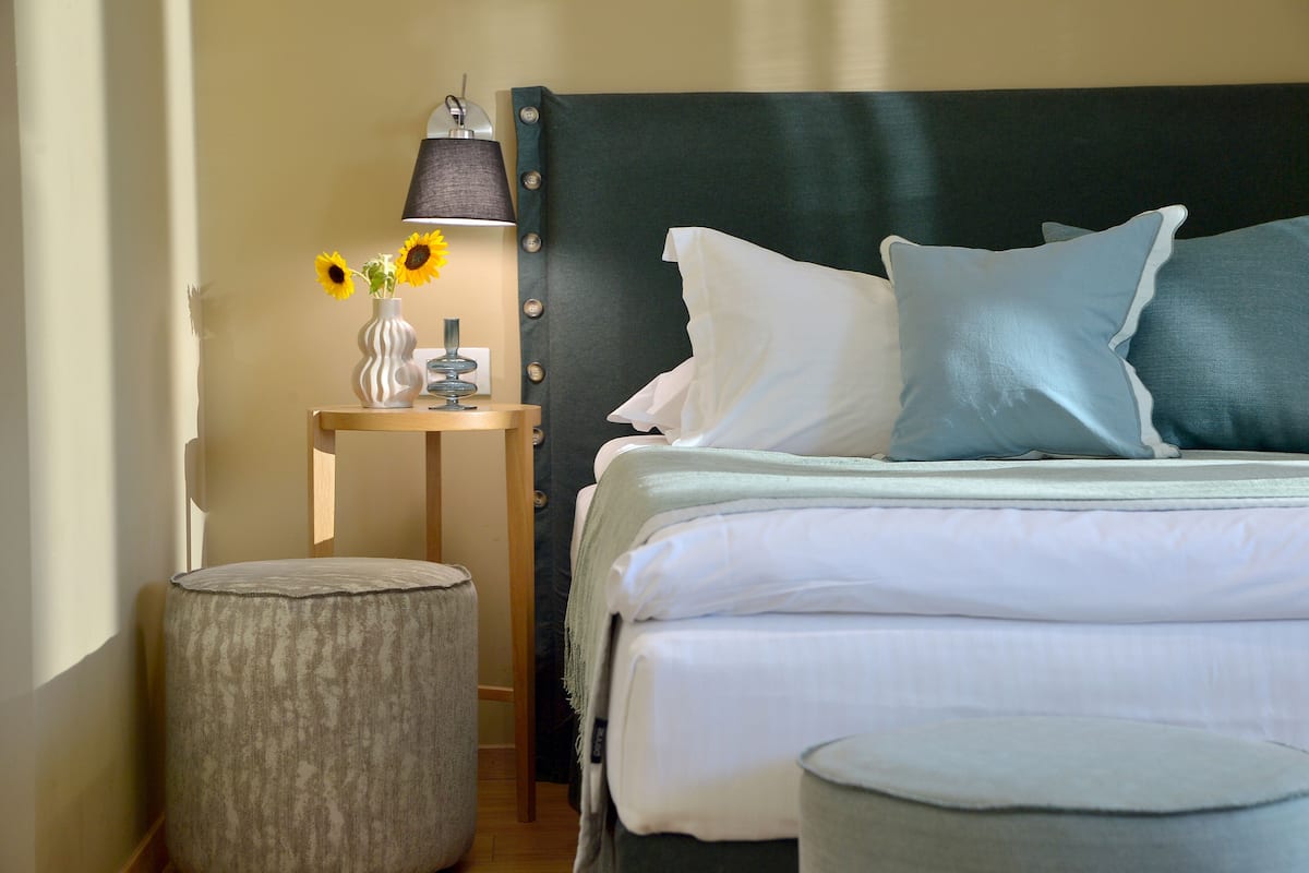 Een netjes opgemaakt bed met kussens, een bedlampje en een vaas met zonnebloemen op een nachtkastje.
