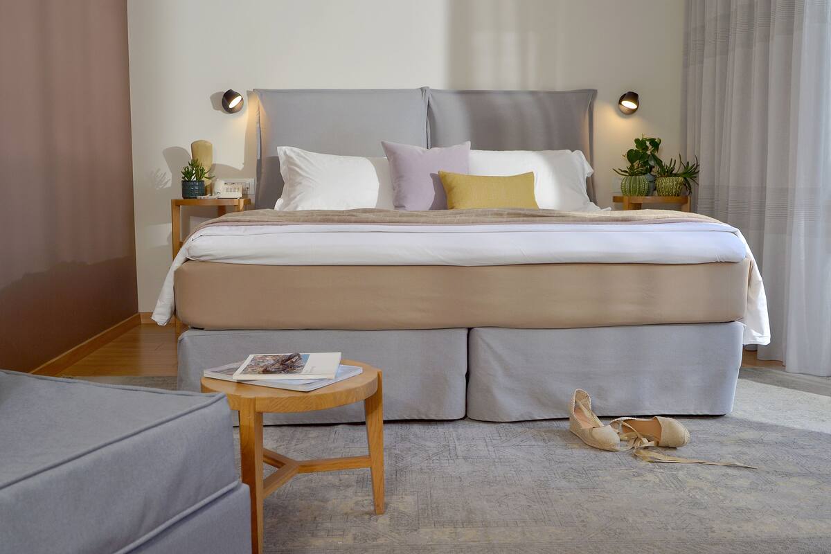 Een moderne slaapkamer met een groot bed, nachtkastjes en een klein tafeltje met een tijdschrift.
