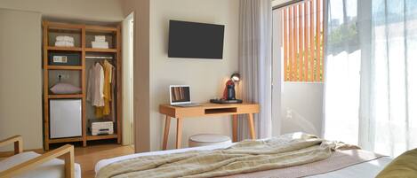 A bedroom with a bed, a desk with a laptop, a wardrobe, and a window with curtains.