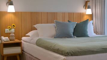 A neatly made bed with white and green bedding, a wooden nightstand with a phone and vase of sunflowers, and two wall-mounted lamps.