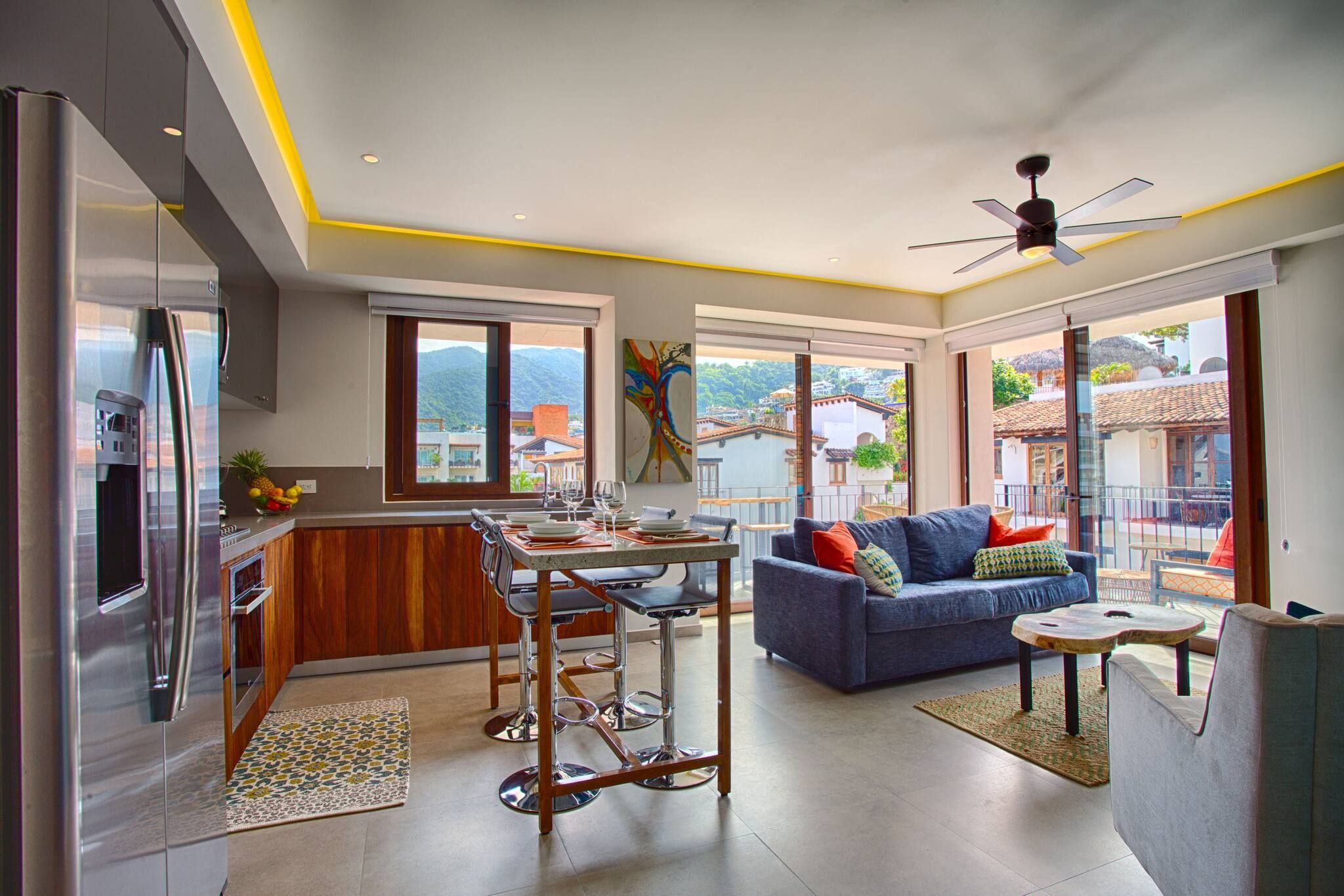 Een moderne keuken met een koelkast, een eethoek met een tafel en stoelen, een bank en een balkon met uitzicht op de stad.