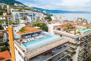 A high-rise hotel with a rooftop infinity pool, multiple balconies, and a view of the sea.